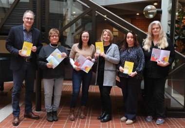 Gruppenbild der Gleichstellungsbeauftragten Inge Keller, Nicole Kruppenbacher, Isabelle Stähle, Sandra Hubert und Marita Rothmann mit Landrat Dietmar Seefeldt vor einem Treppenaufgang im Foyer des Kreishauses der Südlichen Weinstraße in Landau. Alle halten ein Programmhaft der Gleichstellungswochen "Brot und Rosen" 2026 in Händen.