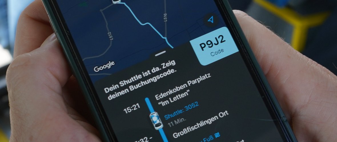 Zwei Hände halten ein Smartphone, auf dem die VRNflexline-App zu sehen ist. Es wird ein Kartenausschnitt angezeigt sowie ein Buchungscode und eine grafische Darstellung des Fahrtverlaufs.