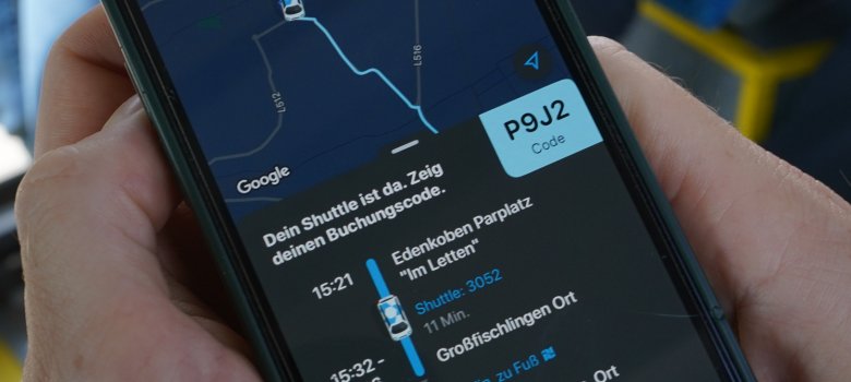 Zwei Hände halten ein Smartphone, auf dem die VRNflexline-App zu sehen ist. Es wird ein Kartenausschnitt angezeigt sowie ein Buchungscode und eine grafische Darstellung des Fahrtverlaufs.