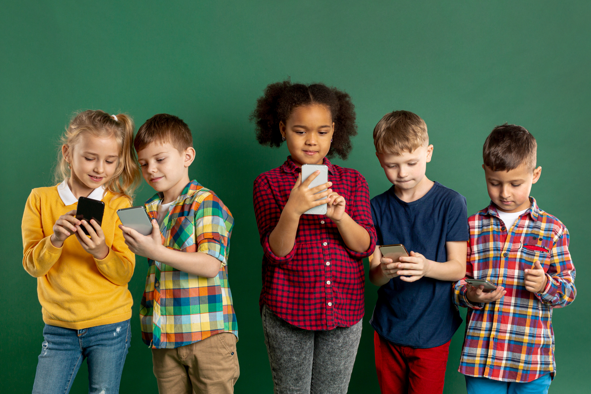 Fünft Kinder stehen nebeneinander vor einem neutralen grünen Hintergrund und schauen jeweils auf ein Smartphone, das sie in Händen halten. Links zeigen sich ein Mädchen und ein Junge gegenseitig etwas auf dem Bildschirm ihres Smarphones.