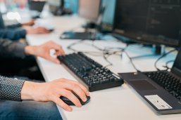 Beschäftigung in Deutschland. Foto: Pixabay Das Bild zeigt eine Person, die an einem Schreibtisch arbeitet und dabei eine Computermaus und eine Tastatur benutzt. Der Fokus liegt auf den Händen der Person: die rechte Hand bedient die Maus, während die linke Hand auf der Tastatur ruht. Im Hintergrund sind verschwommen mehrere Monitore und weitere Arbeitsplätze zu erkennen.