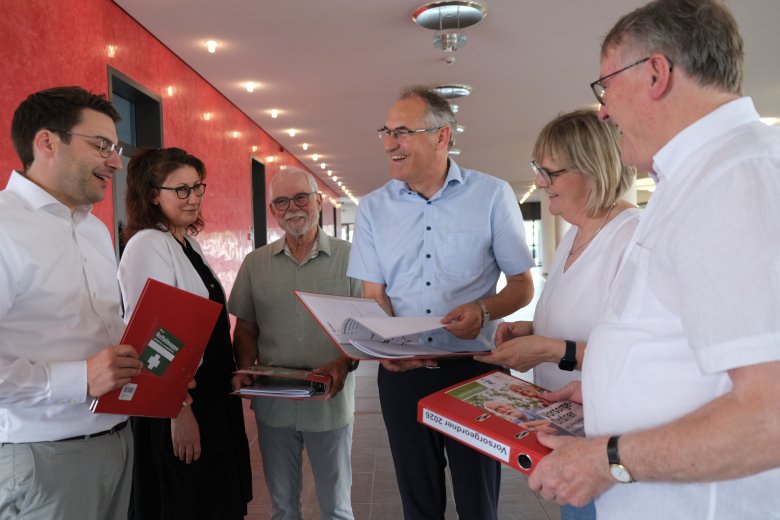 Waren daran beteiligt, dass die neueste Auflage des Vorsorgeordners gedruckt werden kann (von links): Sparkassen-Vorstandsmitglied Benjamin Hirsch, Sonja Bardua vom Referat Demografie der Kreisverwaltung SÜW, Kreisseniorenbeiratsvorsitzender Bernhard Blumenstiel, Landrat Dietmar Seefeldt, Fachkraft Gemeindeschwester plus Ute Wingerter und Kreisseniorenbeiratsmitglied Wolfgang Thiel. Foto: KV SÜW Personen, die sich einen Ordner ansehen.
