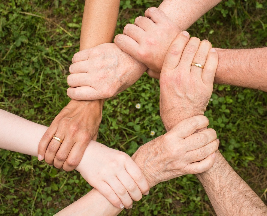 Die Hände mehrerer Personen ergreifen sich gegenseitig am Handgelenk und bilden so einen Kreis als Zeichen der Gemeinschaft.